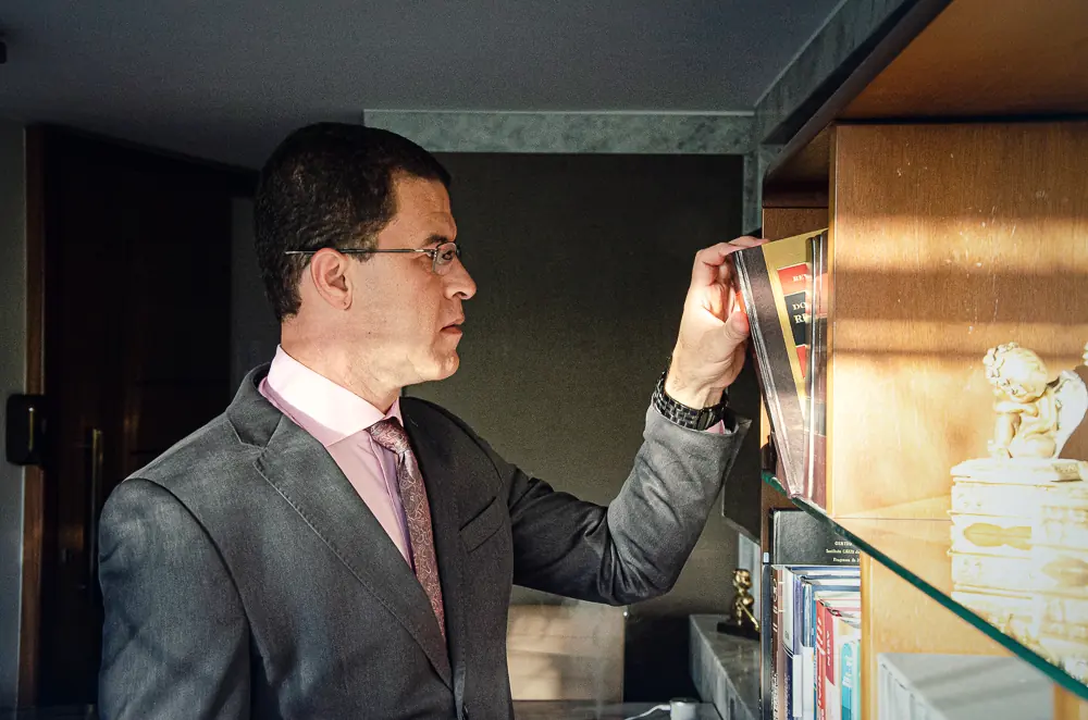 Dr. Márcio Lima da Silva tirando um livro da estante do escritório.